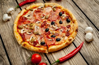 Ahşap arka plan üzerinde mantar, domates, zeytin ve jambon ile taze ev yapımı pizza