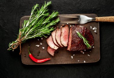 Siyah taş arka plan üzerinde baharat ve biberiye dalları ile Taze ızgara biftek