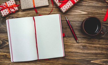 Eski ahşap arka plan üzerinde kırmızı yay ve boş defter ile hediye kutuları yığını 