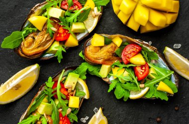 Siyah beton arka plan üzerinde avokado, arugula, mango, domates ve limon dilimleri ile pişmiş midye