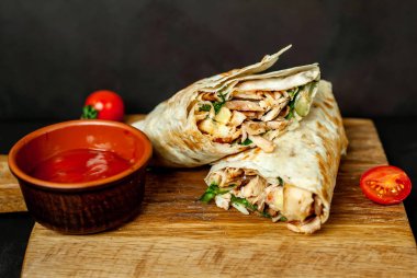 Geleneksel Meksika burrito tavuk ve baharatlı sos ve ahşap doğrama tahtası üzerinde olgun domates ile sarılmış 