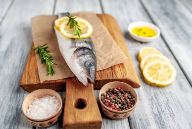 Ahşap doğrama tahtası üzerinde limon dilimleri ve biberiye dalları ile çiğ balık