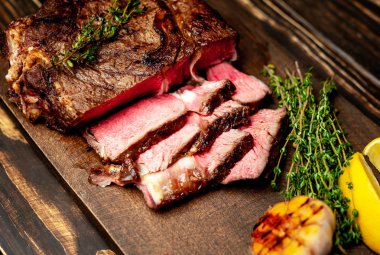 Taze kavrulmuş biftek ahşap doğrama tahtası üzerinde limon dilimleri ve ızgara sarımsak ile servis