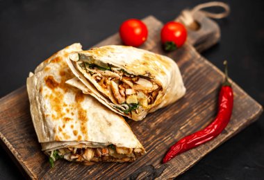 Geleneksel Meksika burrito tavuk ve sebze ile sarılmış ahşap doğrama tahtası üzerinde olgun domates ile servis 