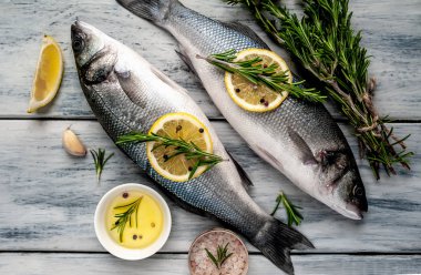 Gri ahşap arka plan üzerinde limon dilimleri ve biberiye dalları ile çiğ balık