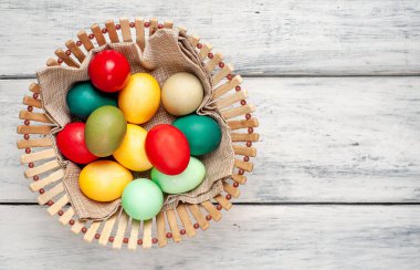 Beyaz ahşap arka plan üzerinde renkli Paskalya ile sepet yumurta