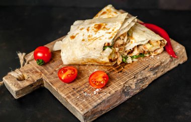 Geleneksel Meksika burrito tavuk ve sebze ile sarılmış ahşap doğrama tahtası üzerinde olgun domates ile servis 