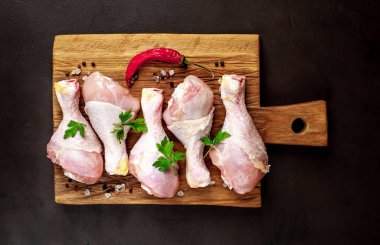 Ahşap doğrama tahtası üzerinde baharat, biber ve maydanoz yaprakları ile Tavuk bacakları 