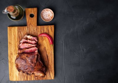 Siyah taş arka plan üzerinde doğrama tahtası üzerinde baharat ve biber ile Yağlı ızgara domuz biftek