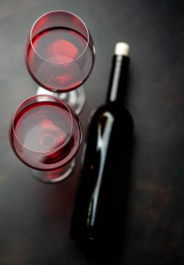 Siyah arka planda iki bardak kırmızı şarap ve şarap şişesi