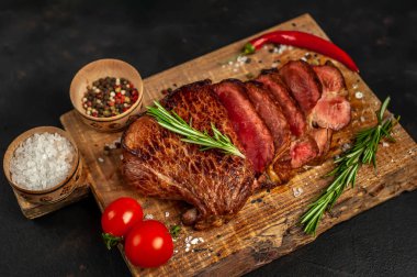 Taze sığır eti biftek ahşap tahta üzerinde domates, biberiye biberiye ve biberiye dalları ile servis