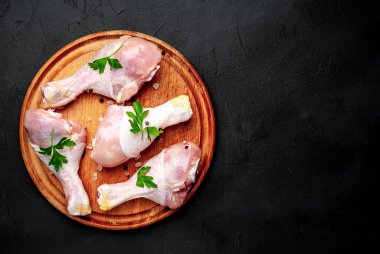 Baharat, tuz ve maydanoz siyah taş arka plan üzerinde yuvarlak ahşap tahta üzerinde yaprakları ile Tavuk bacakları