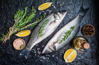 Siyah taş arka plan üzerinde limon, baharat ve biberiye dalları ile çiğ balık