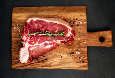 Taş arka plan üzerinde ahşap doğrama tahtası üzerinde baharat ve biberiye dal ile Çiğ yağlı biftek