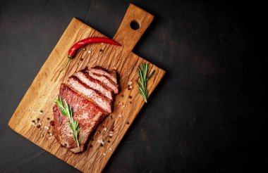Siyah taş arka plan üzerinde ahşap doğrama tahtası üzerinde baharat ve biberiye dalları ile Taze ızgara domuz biftek