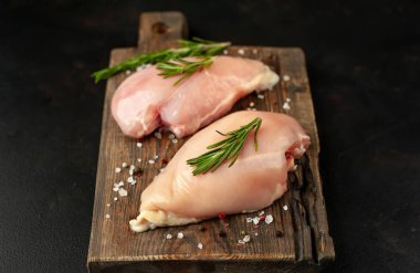 Ahşap doğrama tahtası üzerinde tuz ve biberiye dalları ile Çiğ tavuk fileto