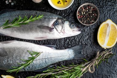 Siyah taş arka plan üzerinde limon, baharat ve biberiye dalları ile çiğ balık