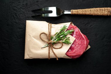 Çiğ sığır eti biftek taş arka plan üzerinde biberiye dalları ile zanaat kağıt sarılmış 