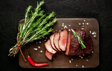 Siyah taş arka plan üzerinde baharat ve biberiye dalları ile Taze ızgara biftek