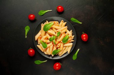 domates soslu makarna, yeşil yapraklar ve taş siyah arka plan üzerinde olgun domates