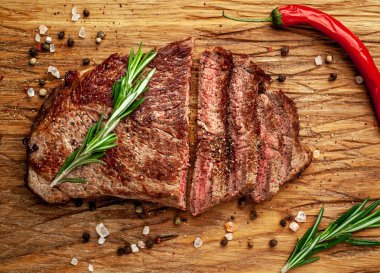 Siyah taş arka plan üzerinde ahşap doğrama tahtası üzerinde baharat ve biberiye dalları ile Taze ızgara domuz biftek