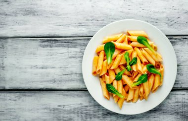 Ahşap arka plan üzerinde domates sosu ve yeşil yaprakları ile Makarna 