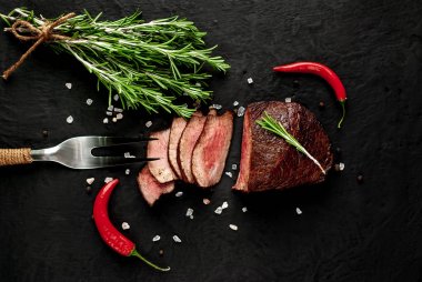 Siyah taş arka plan üzerinde baharat ve biberiye dalları ile Taze ızgara biftek