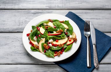 Ahşap arka plan üzerinde ıspanak yaprakları, peynir, nar tohumu, elma dilimleri ve fındık ile taze salata 