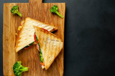 Ahşap doğrama tahtasında jambon, taze brokoli ve peynirile taze ızgara sandviçler