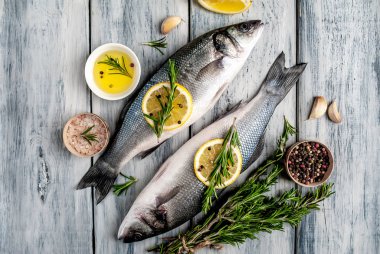 Gri ahşap arka plan üzerinde limon dilimleri ve biberiye dalları ile çiğ balık