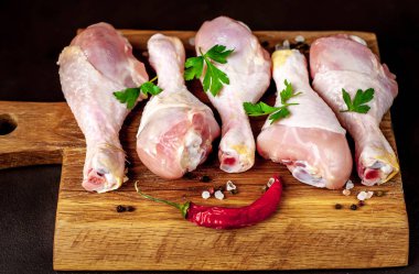 Ahşap doğrama tahtası üzerinde baharat, biber ve maydanoz yaprakları ile Tavuk bacakları 