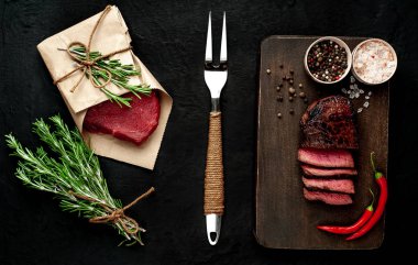 Dilimlenmiş biftek ve çiğ biftek siyah taş arka plan üzerinde zanaat kağıt sarılmış