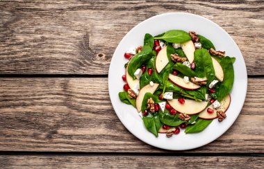 Ahşap arka plan üzerinde ıspanak yaprakları, peynir, nar tohumu, elma dilimleri ve fındık ile taze salata 