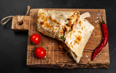 Geleneksel Meksika burrito tavuk ve sebze ile sarılmış ahşap doğrama tahtası üzerinde olgun domates ile servis 