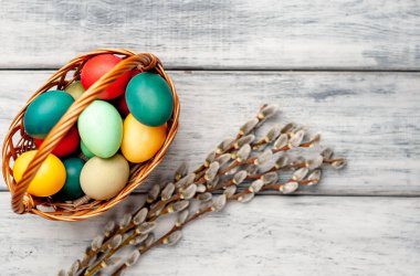 Beyaz ahşap arka planda renkli Paskalya yumurtaları ve kedi söğüt dalları ile sepet