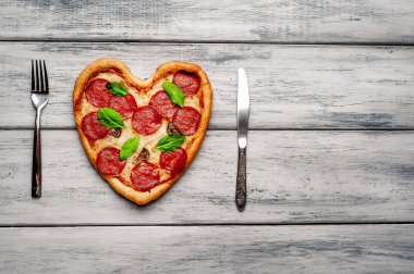 ahşap arka plan üzerinde salam ve taze fesleğen yaprakları ile peynir kalp pizza