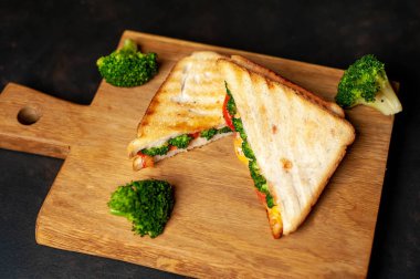 Ahşap doğrama tahtasında jambon, taze brokoli ve peynirile taze ızgara sandviçler
