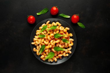 domates soslu makarna, yeşil yapraklar ve taş siyah arka plan üzerinde olgun domates