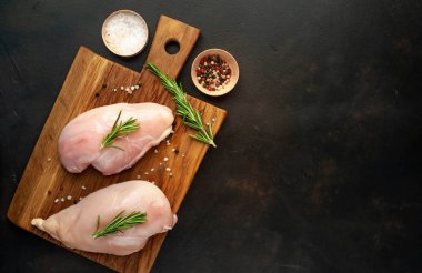 Ahşap doğrama tahtası üzerinde tuz ve biberiye dalları ile Çiğ tavuk fileto