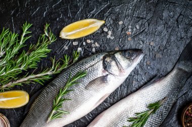 Siyah taş arka plan üzerinde limon, baharat ve biberiye dalları ile çiğ balık