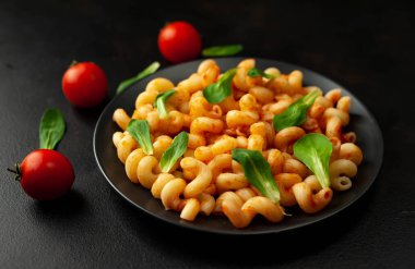 domates soslu makarna, yeşil yapraklar ve taş siyah arka plan üzerinde olgun domates
