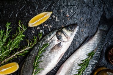 Siyah taş arka plan üzerinde limon, baharat ve biberiye dalları ile çiğ balık