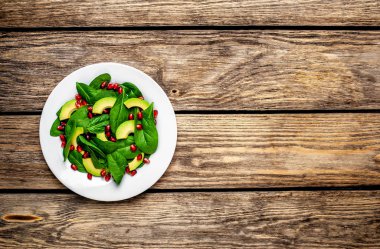 Ahşap masada ıspanak yaprakları, avokado dilimleri ve nar taneleri ile taze yeşil salata 