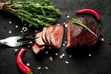 Siyah taş arka plan üzerinde baharat ve biberiye dalları ile Taze ızgara biftek