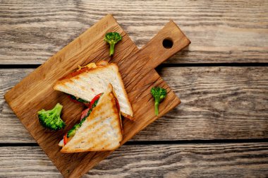 Ahşap doğrama tahtasında jambon, taze brokoli ve peynirile taze ızgara sandviçler