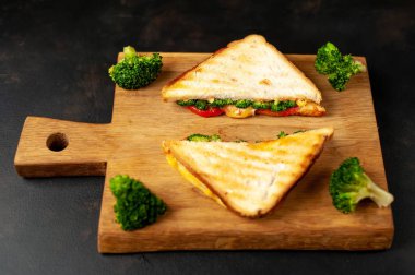 Ahşap doğrama tahtasında jambon, taze brokoli ve peynirile taze ızgara sandviçler