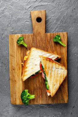 Ahşap doğrama tahtasında jambon, taze brokoli ve peynirile taze ızgara sandviçler