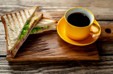 Jambon ve peynir ile taze ızgara sandviç ahşap doğrama tahtası üzerinde kahve fincan ile servis