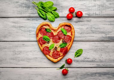 salam, taze fesleğen yaprakları ve ahşap arka plan üzerinde olgun kiraz domates ile peynir kalp pizza 