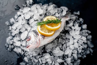 Soğuk ezilmiş buz yığını üzerinde limon dilimleri ve biberiye ile taze balık yakın görünümü